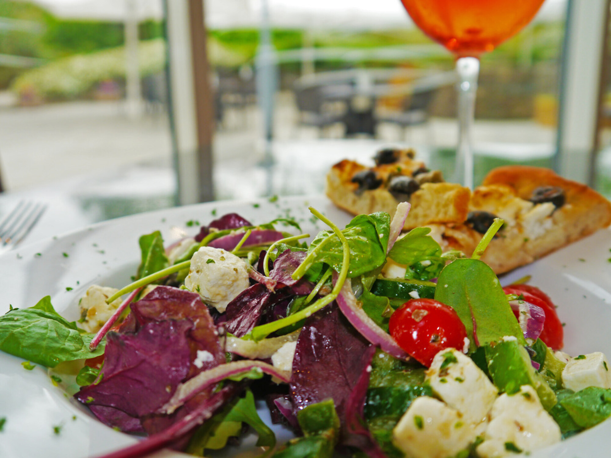 Lunch and Evening Menu: Greek Salad; feta cheese, vine cherry tomatoes, cucumber, red onion, black olives, green peppers, oregano, lemon and extra virgin olive oil dressing served with homemade warm focaccia bread (v) £10.50